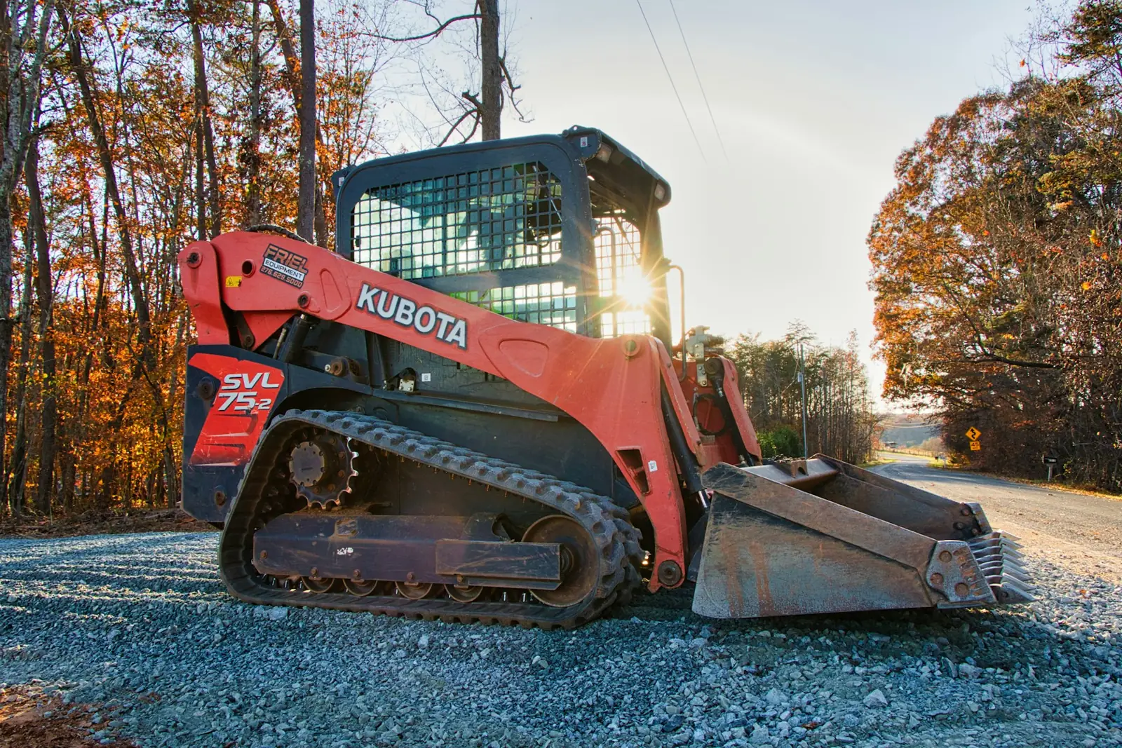 Compact track loader on a gravel drive at sunrise